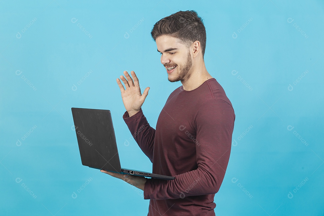 Homem jovem segurando notebook sobre fundo isolado azul.
