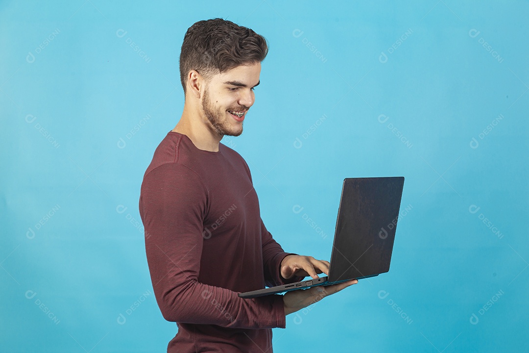 Homem jovem segurando notebook sobre fundo isolado azul.