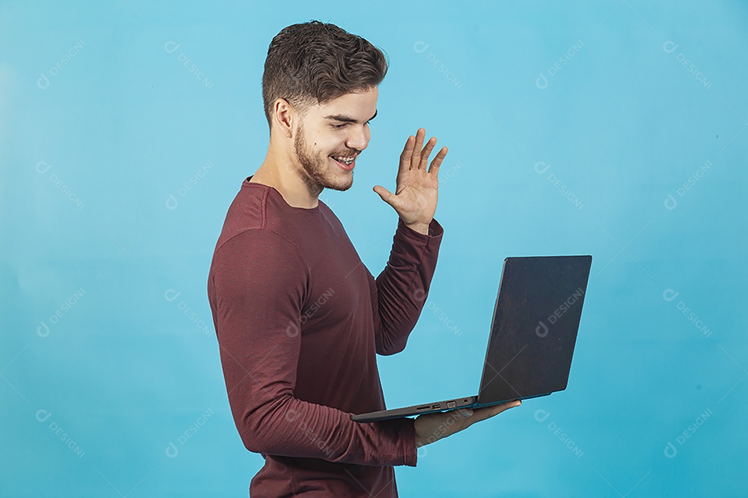 Homem jovem segurando notebook sobre fundo isolado azul.