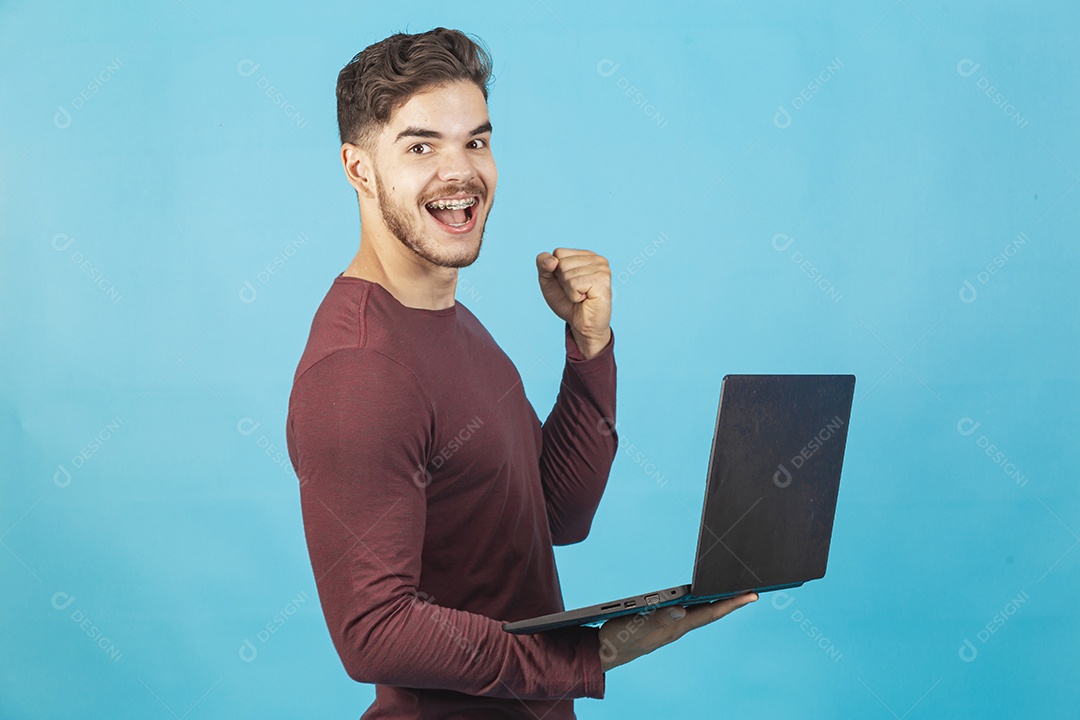 Homem jovem segurando notebook sobre fundo isolado azul.