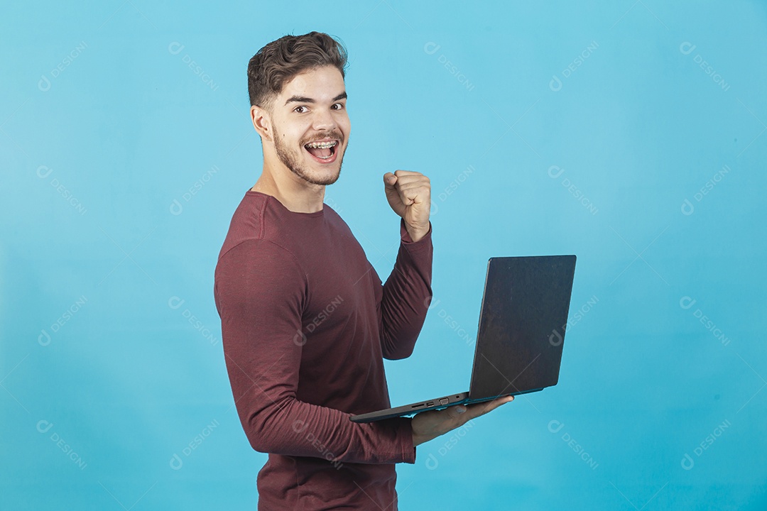 Homem jovem segurando notebook sobre fundo isolado azul.