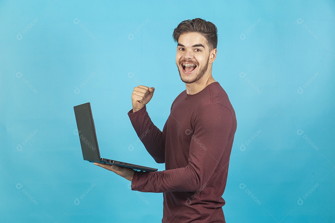 Homem jovem segurando notebook sobre fundo isolado azul.