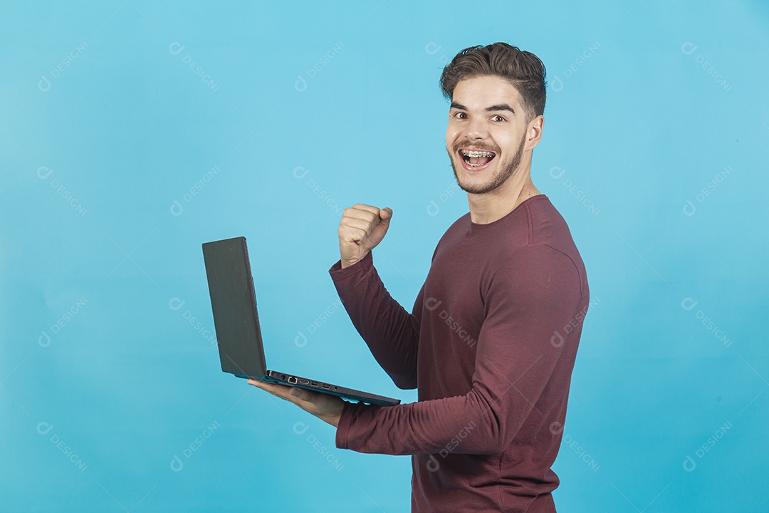 Homem jovem segurando notebook sobre fundo isolado azul.