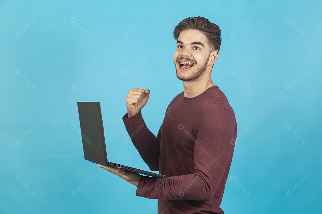 Homem jovem segurando notebook sobre fundo isolado azul.