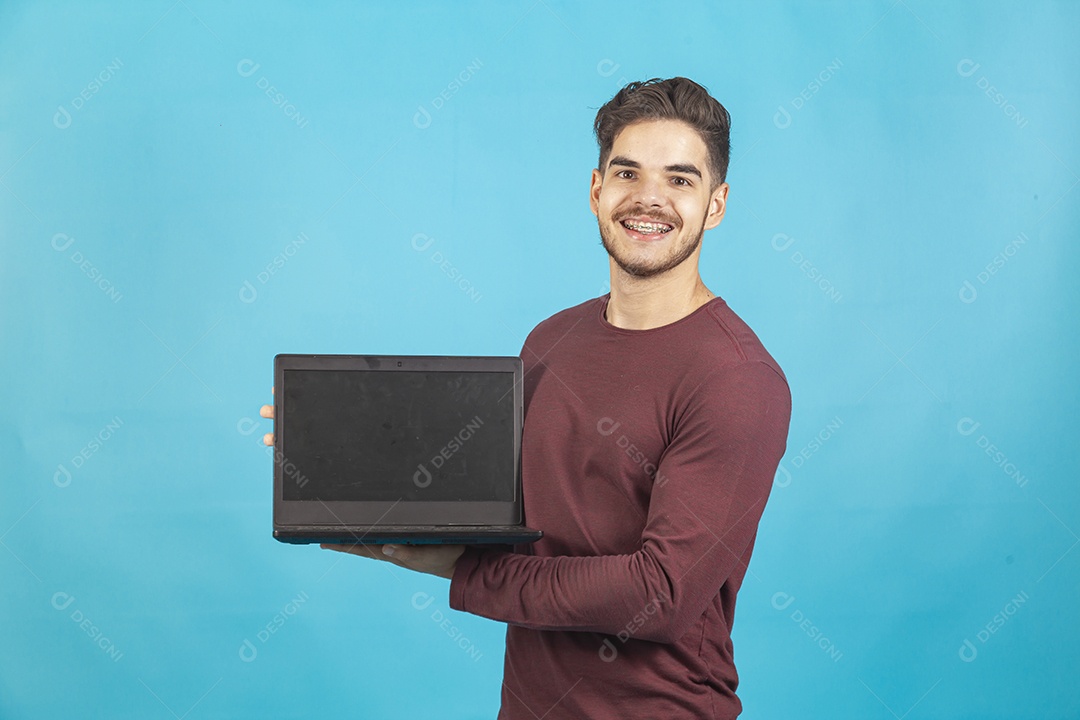 Homem jovem segurando notebook sobre fundo isolado azul.