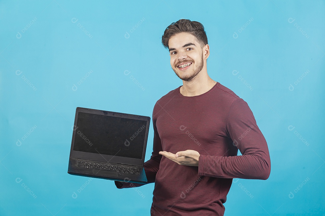 Homem jovem segurando notebook sobre fundo isolado azul.