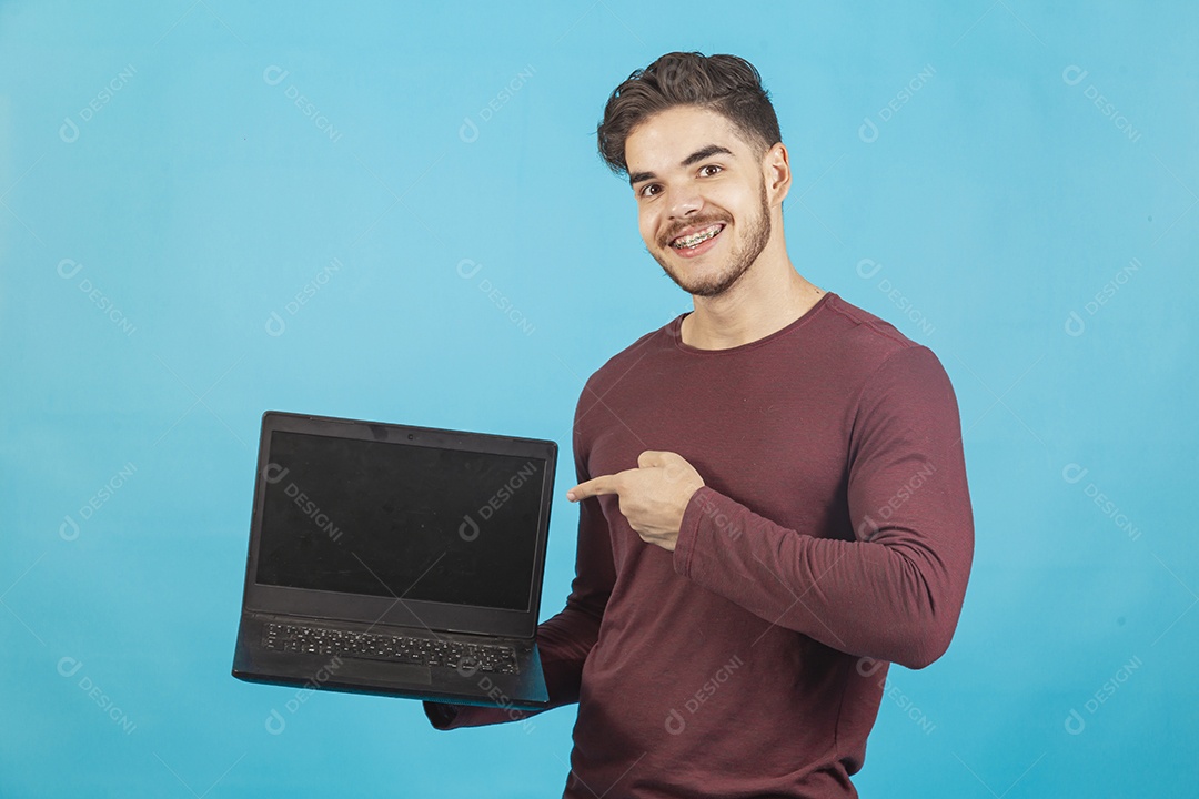 Homem jovem segurando notebook sobre fundo isolado azul.