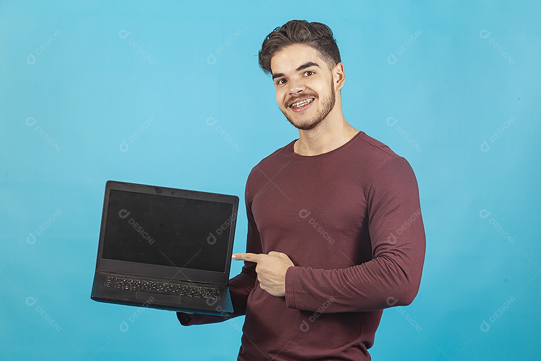 Homem jovem segurando notebook sobre fundo isolado azul.