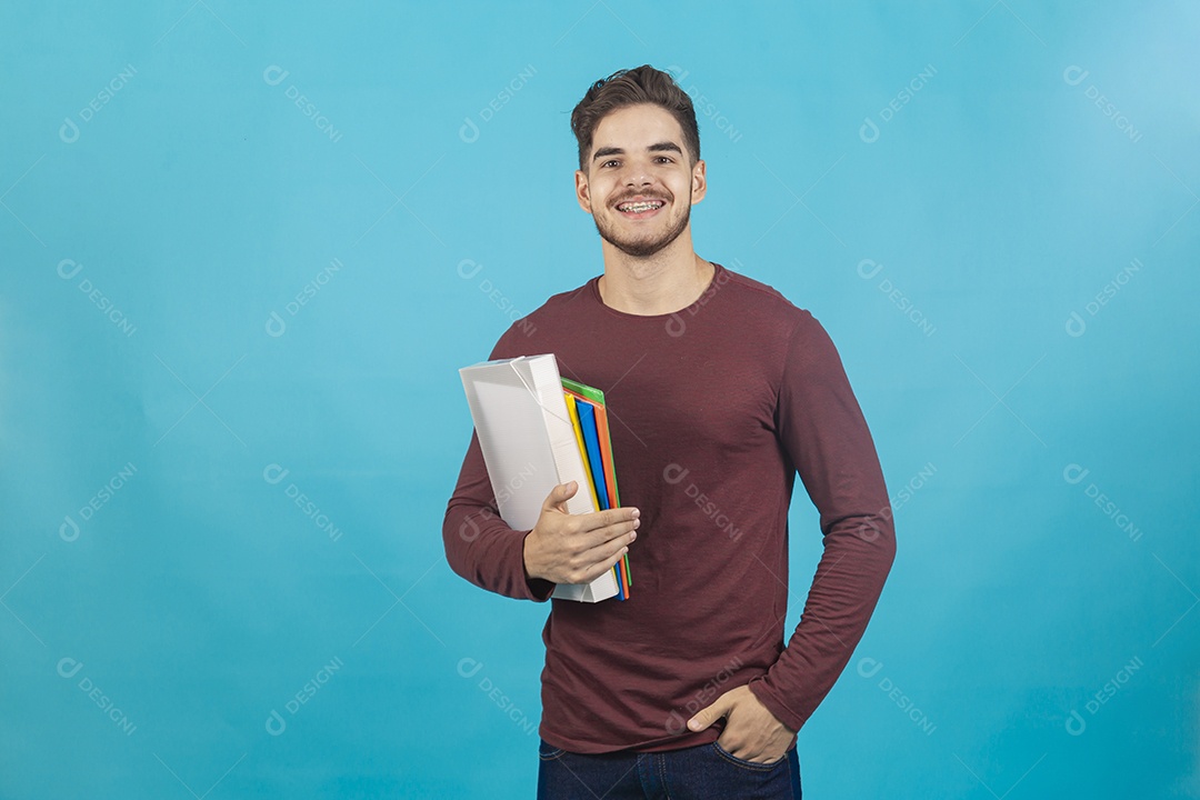 Homem jovem segurando livros sobre fundo isolado azul.