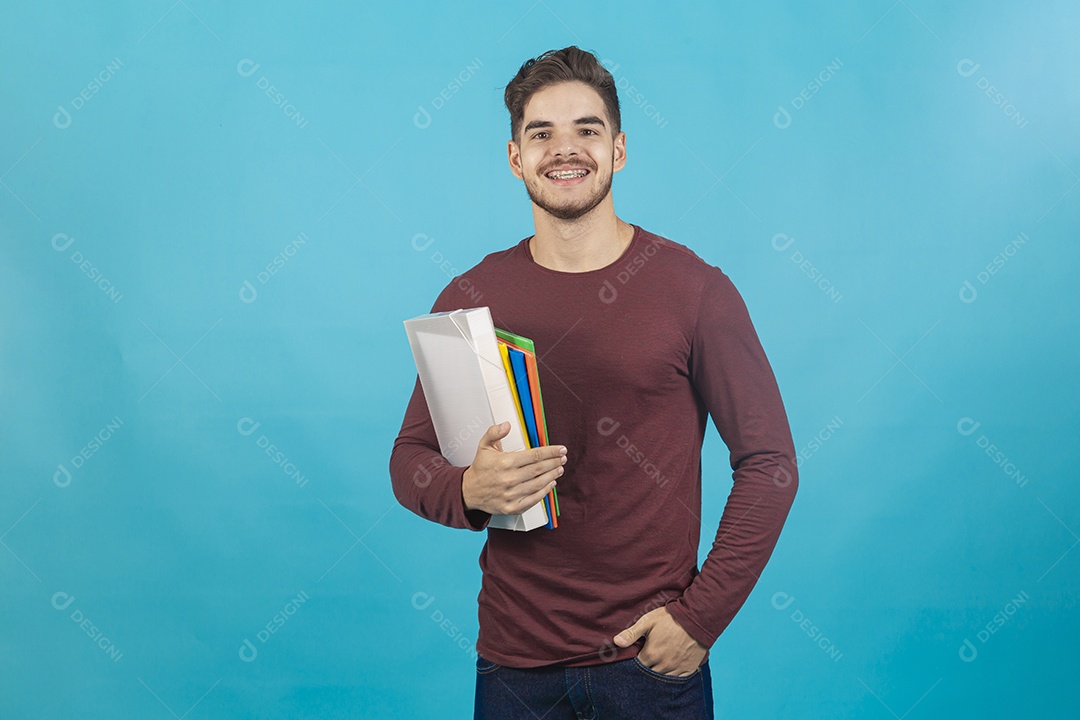 Homem jovem segurando livros sobre fundo isolado azul.