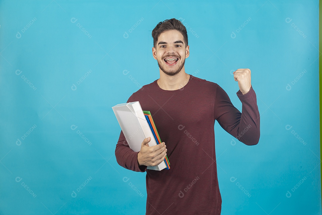 Homem jovem segurando livros sobre fundo isolado azul.