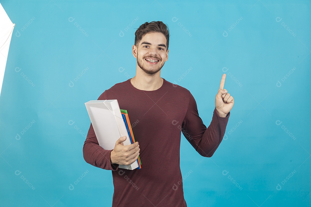 Homem jovem segurando livros sobre fundo isolado azul.
