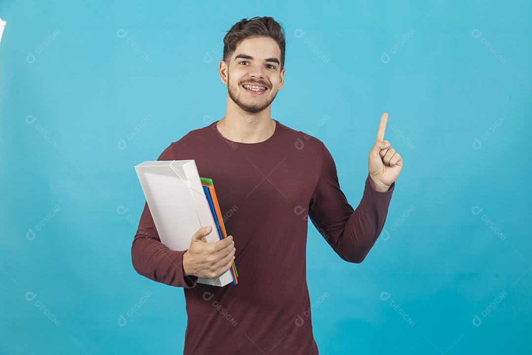 Homem jovem segurando livros sobre fundo isolado azul.
