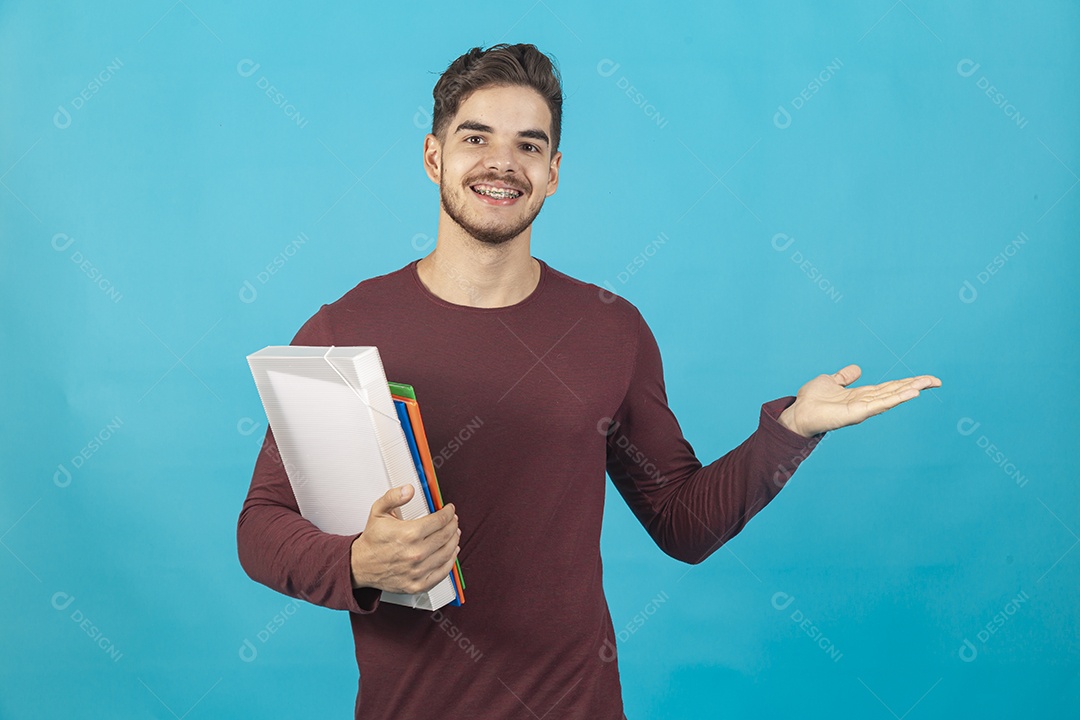 Homem jovem segurando livros sobre fundo isolado azul.