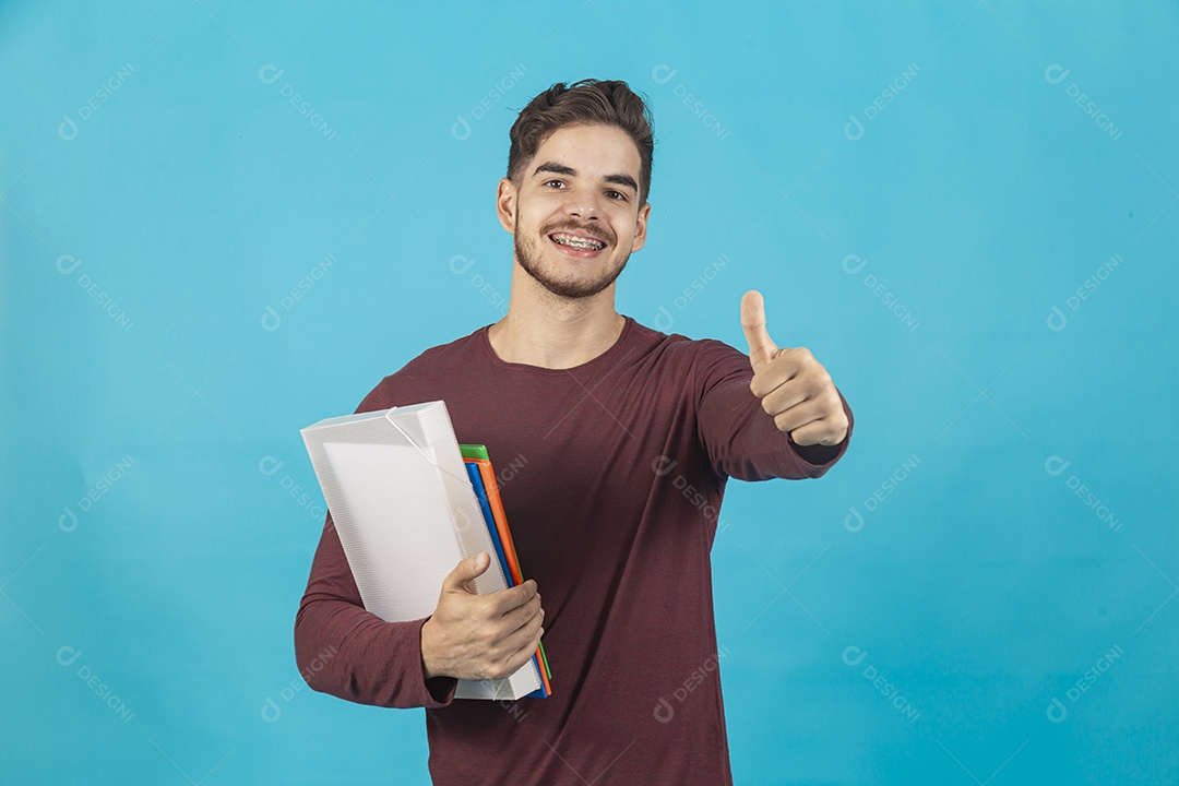 Homem jovem segurando livros sobre fundo isolado azul.
