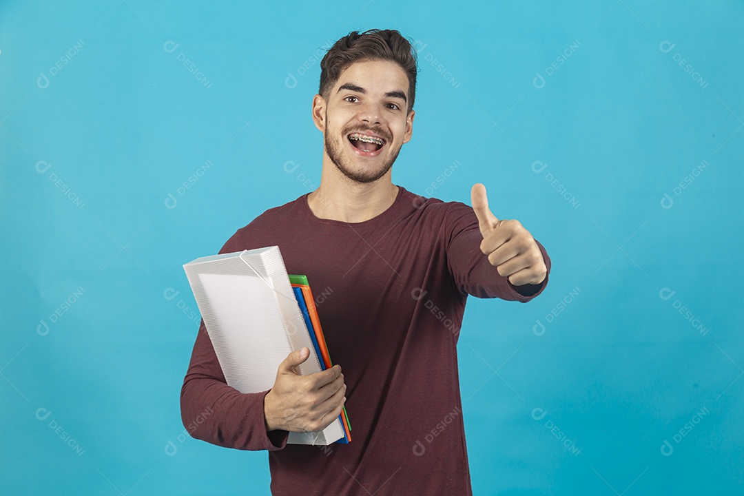 Homem jovem segurando livros sobre fundo isolado azul.
