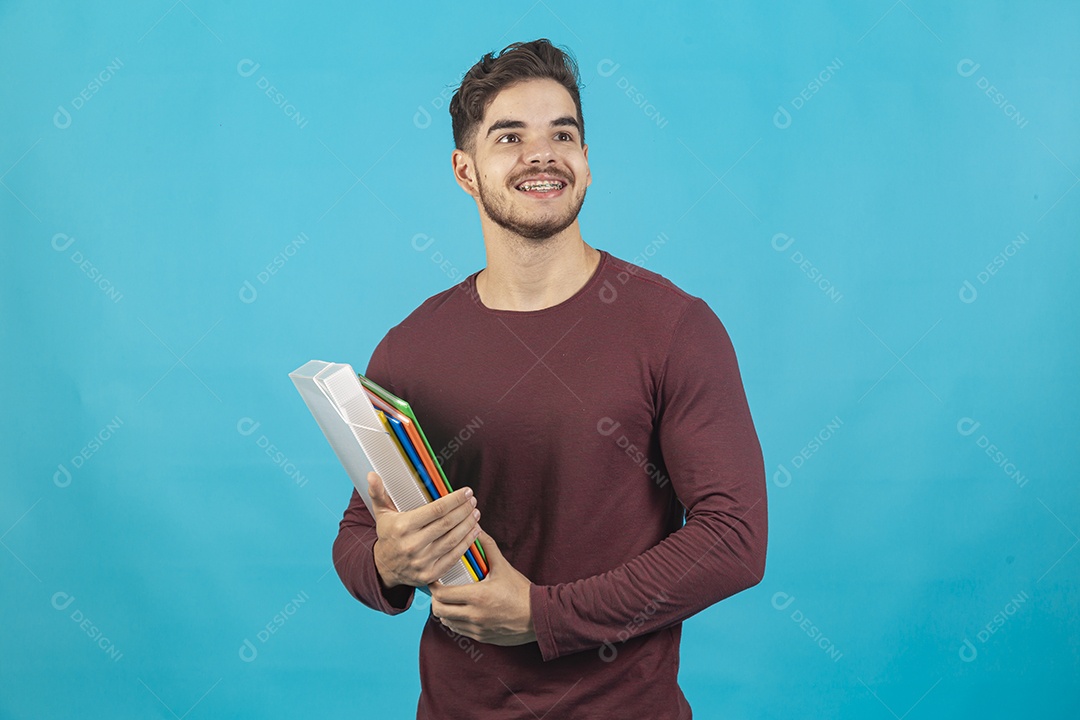 Homem jovem segurando livros sobre fundo isolado azul.