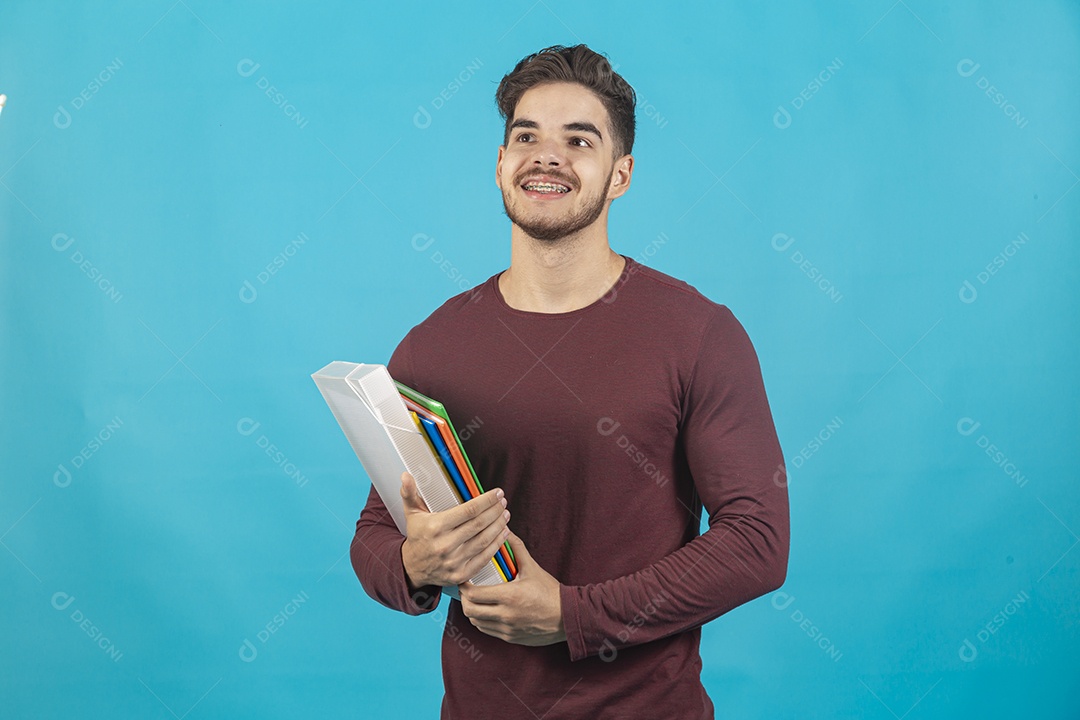 Homem jovem segurando livros sobre fundo isolado azul.