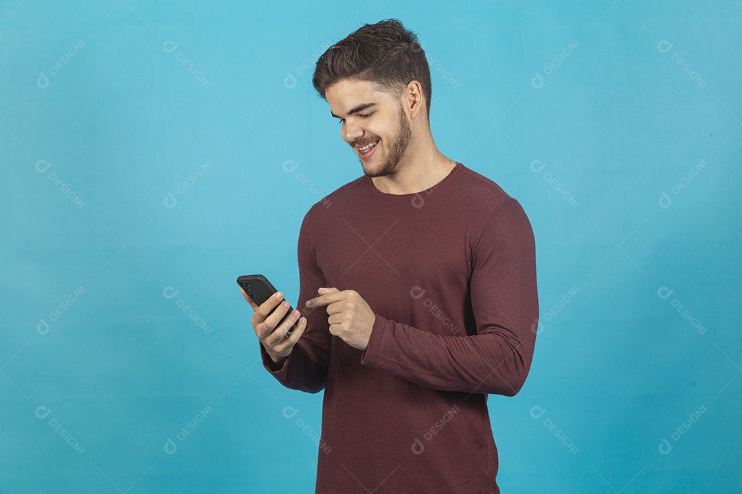 Homem jovem segurando celular sobre fundo isolado azul.