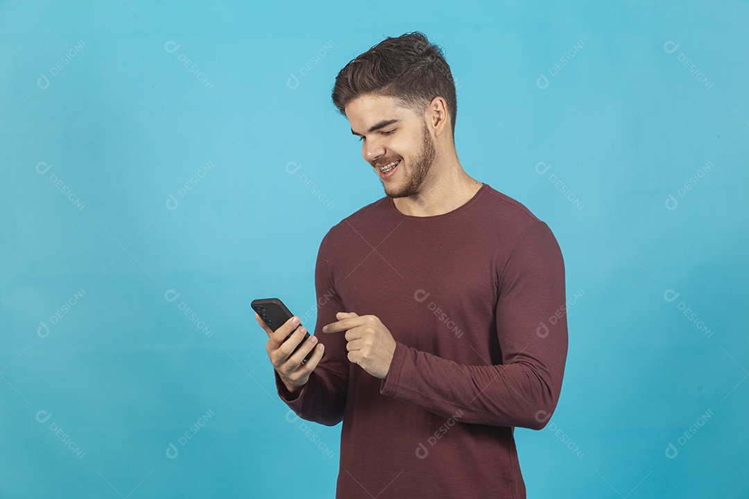 Homem jovem segurando celular sobre fundo isolado azul.