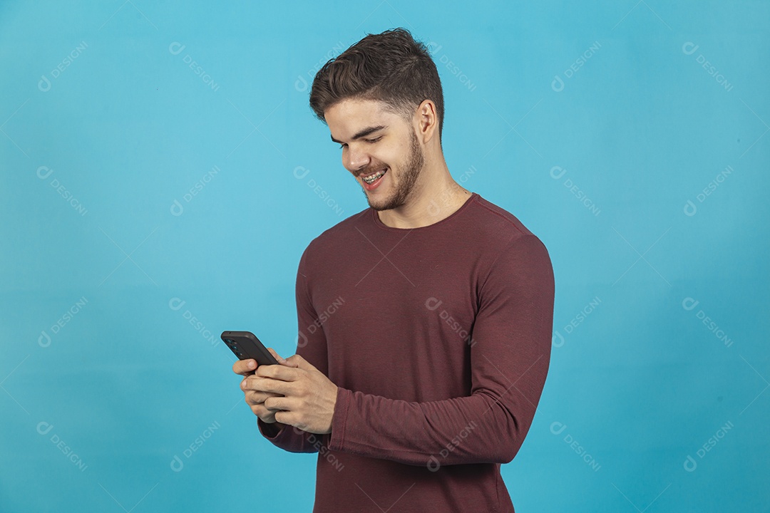 Homem jovem segurando celular sobre fundo isolado azul.
