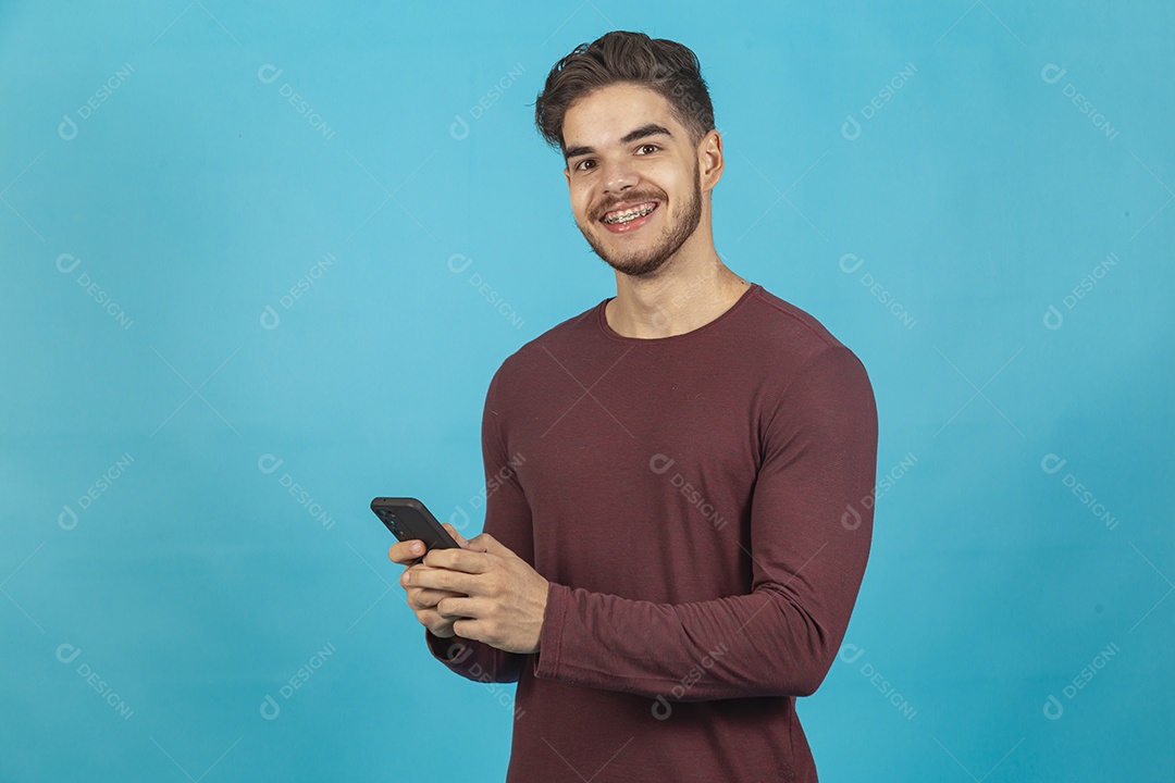 Homem jovem segurando celular sobre fundo isolado azul.