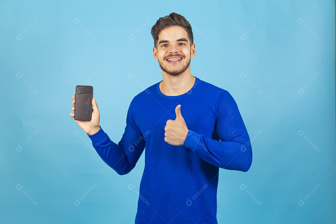 Homem sorridente segurando celular sobre um fundo isolado azul.