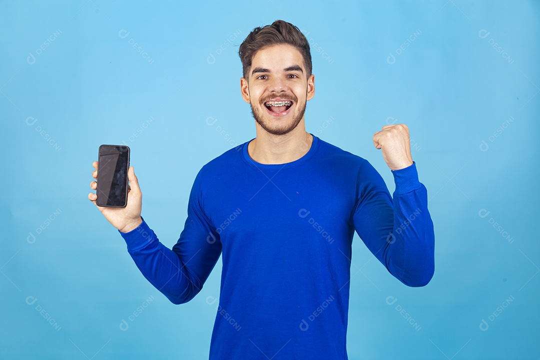 Homem sorridente segurando celular sobre um fundo isolado azul.