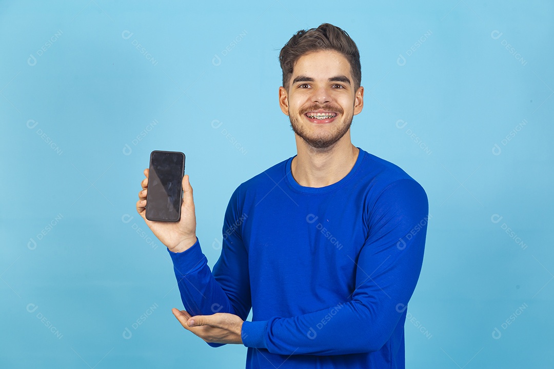 Homem sorridente segurando celular sobre um fundo isolado azul.