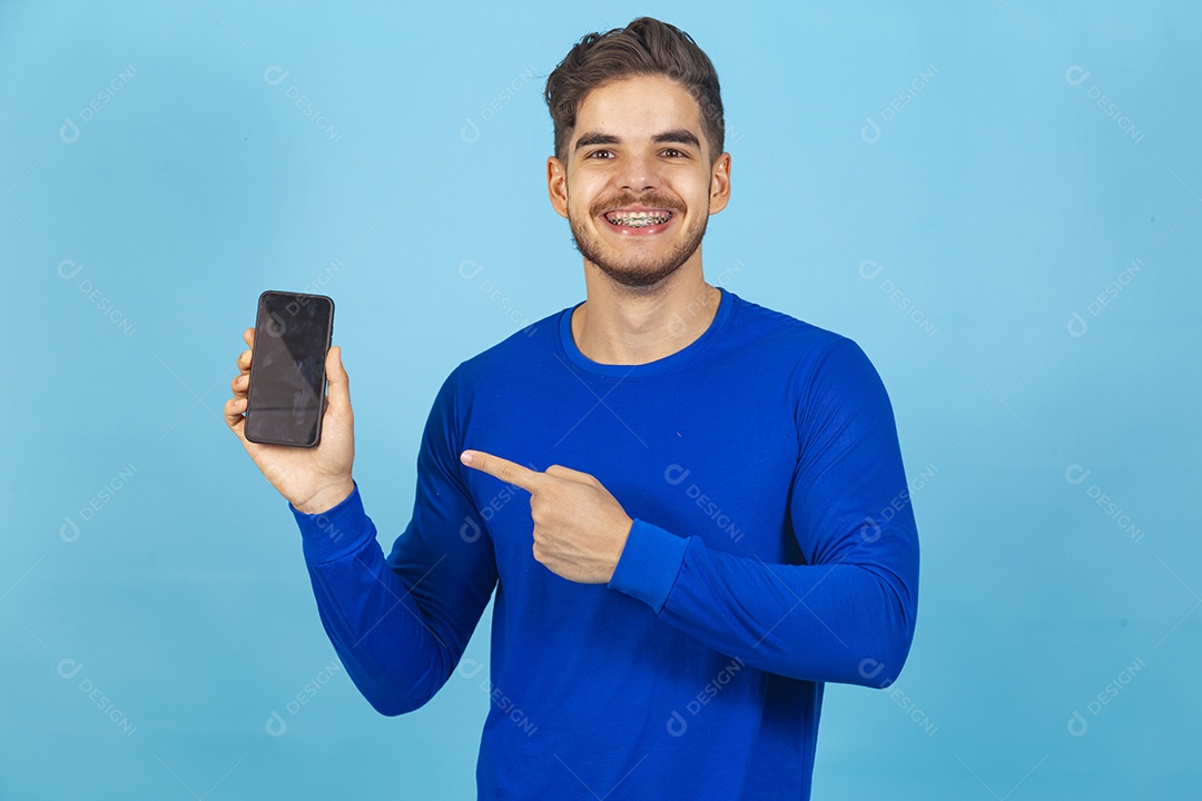 Homem sorridente segurando celular sobre um fundo isolado azul.