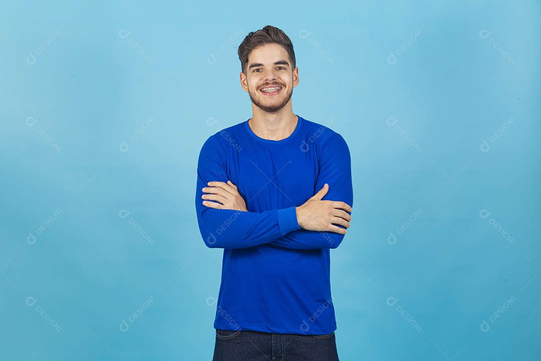 Homem sorridente de braços cruzados sobre um fundo isolado azul.