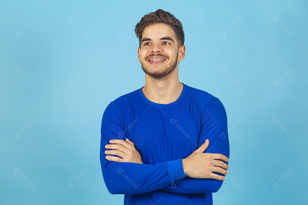 Homem sorridente de braços cruzados sobre um fundo isolado azul.