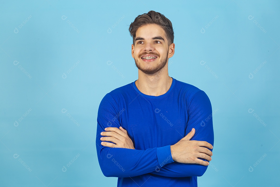 Homem sorridente de braços cruzados sobre um fundo isolado azul.