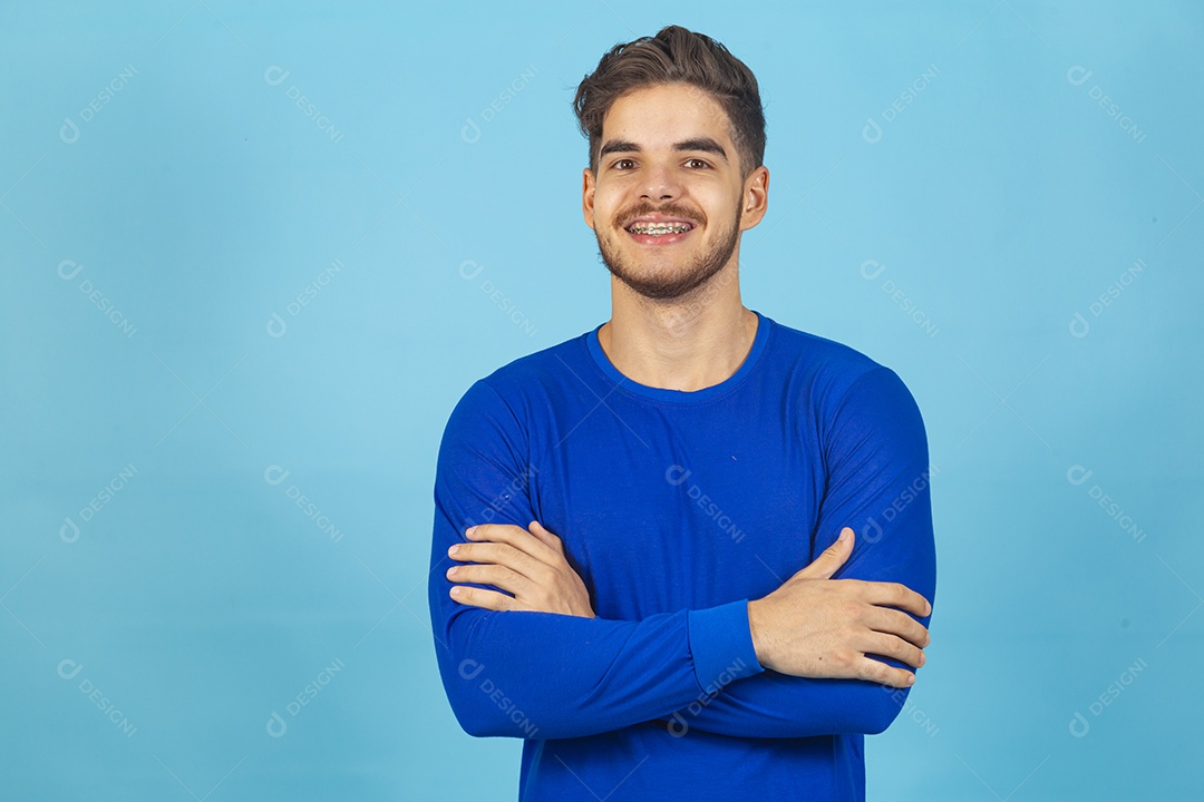 Homem sorridente de braços cruzados sobre um fundo isolado azul.