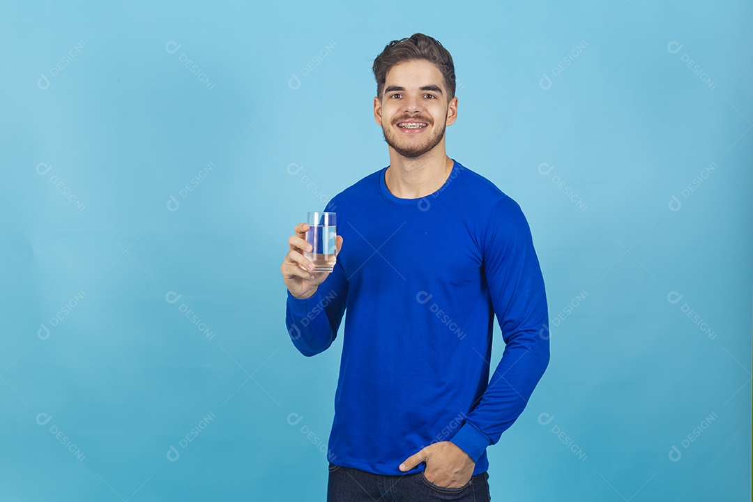 Homem sorridente segurando copo com água sobre um fundo isolado azul.