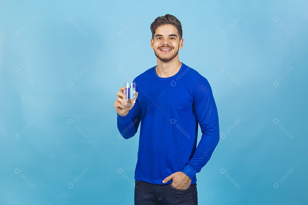 Homem sorridente segurando copo com água sobre um fundo isolado azul.