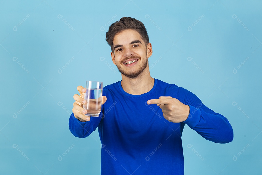 Homem sorridente segurando copo com água sobre um fundo isolado azul.