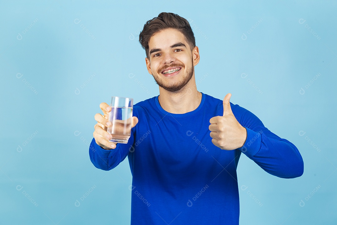 Homem sorridente segurando copo com água sobre um fundo isolado azul.