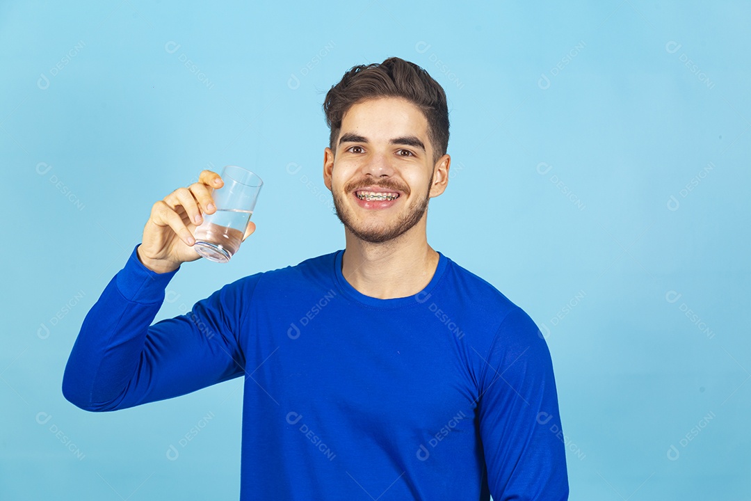 Homem sorridente segurando copo com água sobre um fundo isolado azul.