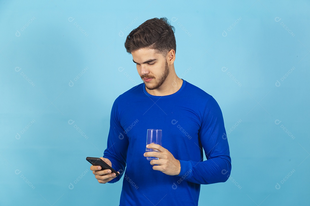 Homem segurando copo e olhando o celular sobre um fundo isolado azul.