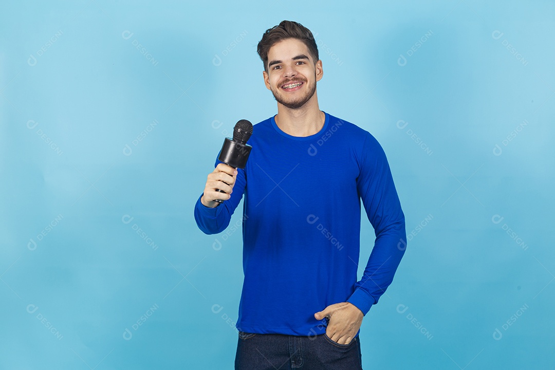 Homem sorridente segurando microfone sobre um fundo isolado azul.