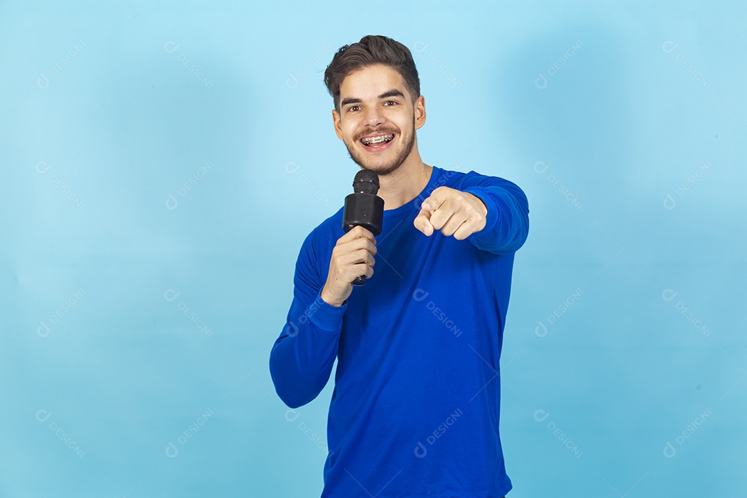 Homem sorridente segurando microfone sobre um fundo isolado azul.