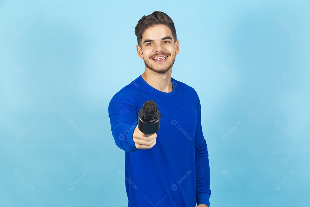 Homem sorridente segurando microfone sobre um fundo isolado azul.