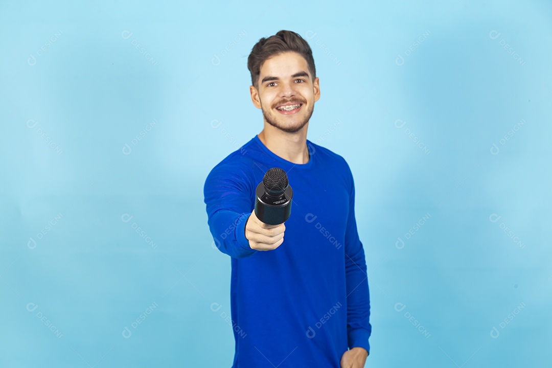 Homem sorridente segurando microfone sobre um fundo isolado azul.