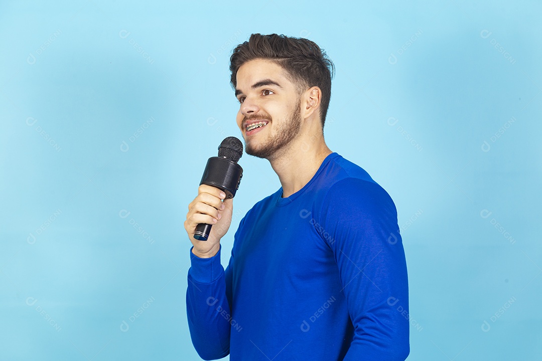 Homem sorridente segurando microfone sobre um fundo isolado azul.