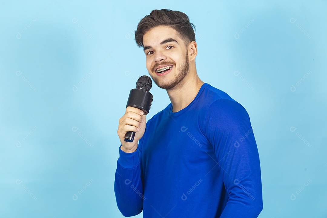 Homem sorridente segurando microfone sobre um fundo isolado azul.