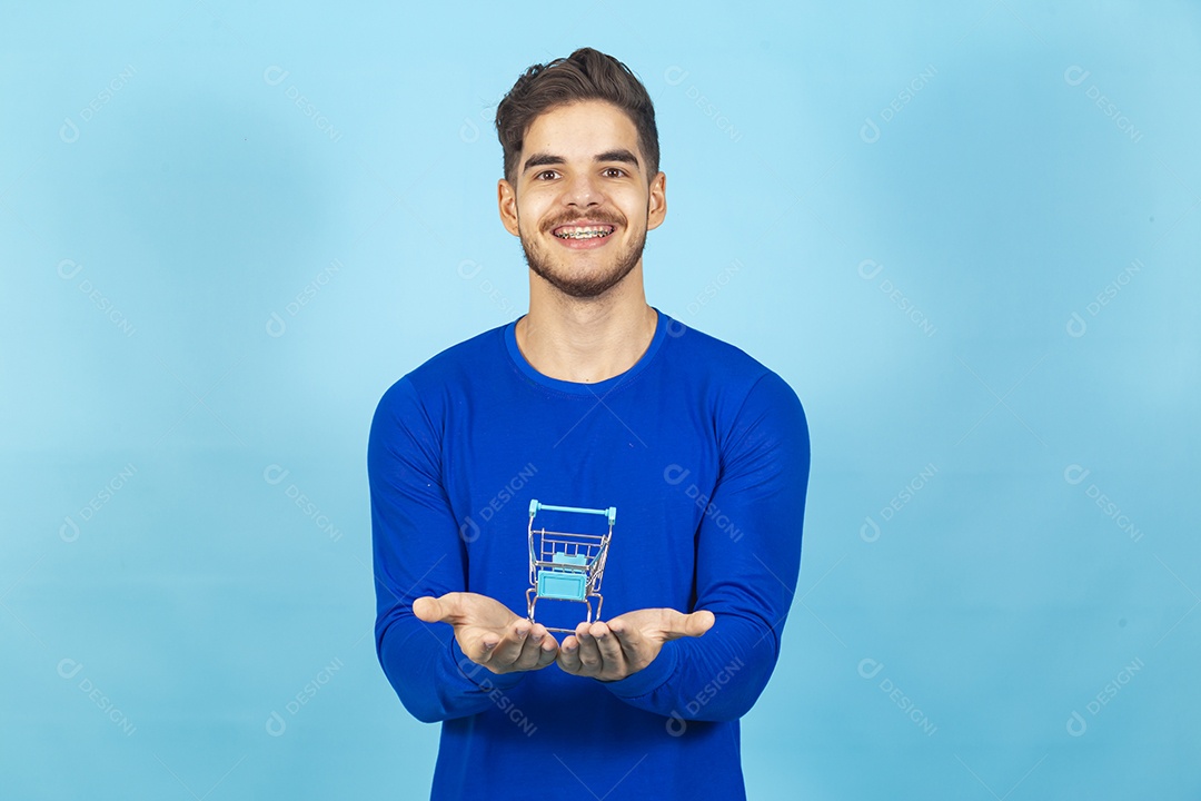 Homem sorridente com mini carrinho de supermercado sobre as mãos.