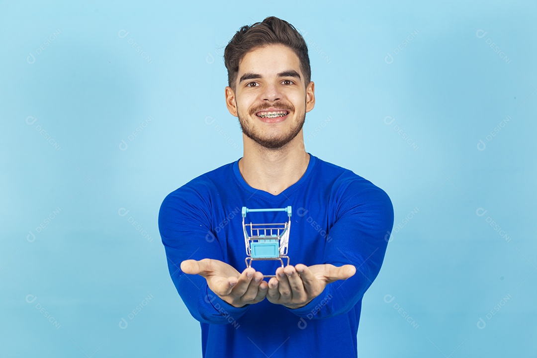 Homem sorridente com mini carrinho de supermercado sobre as mãos.