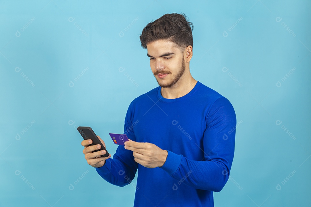 Homem segurando cartão e celular sobre um fundo isolado azul.
