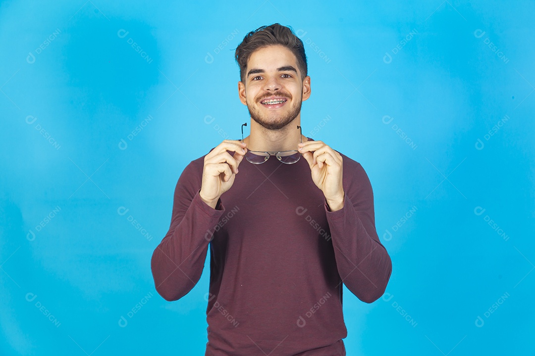 Homem sorridente segurando óculos sobre um fundo isolado azul.